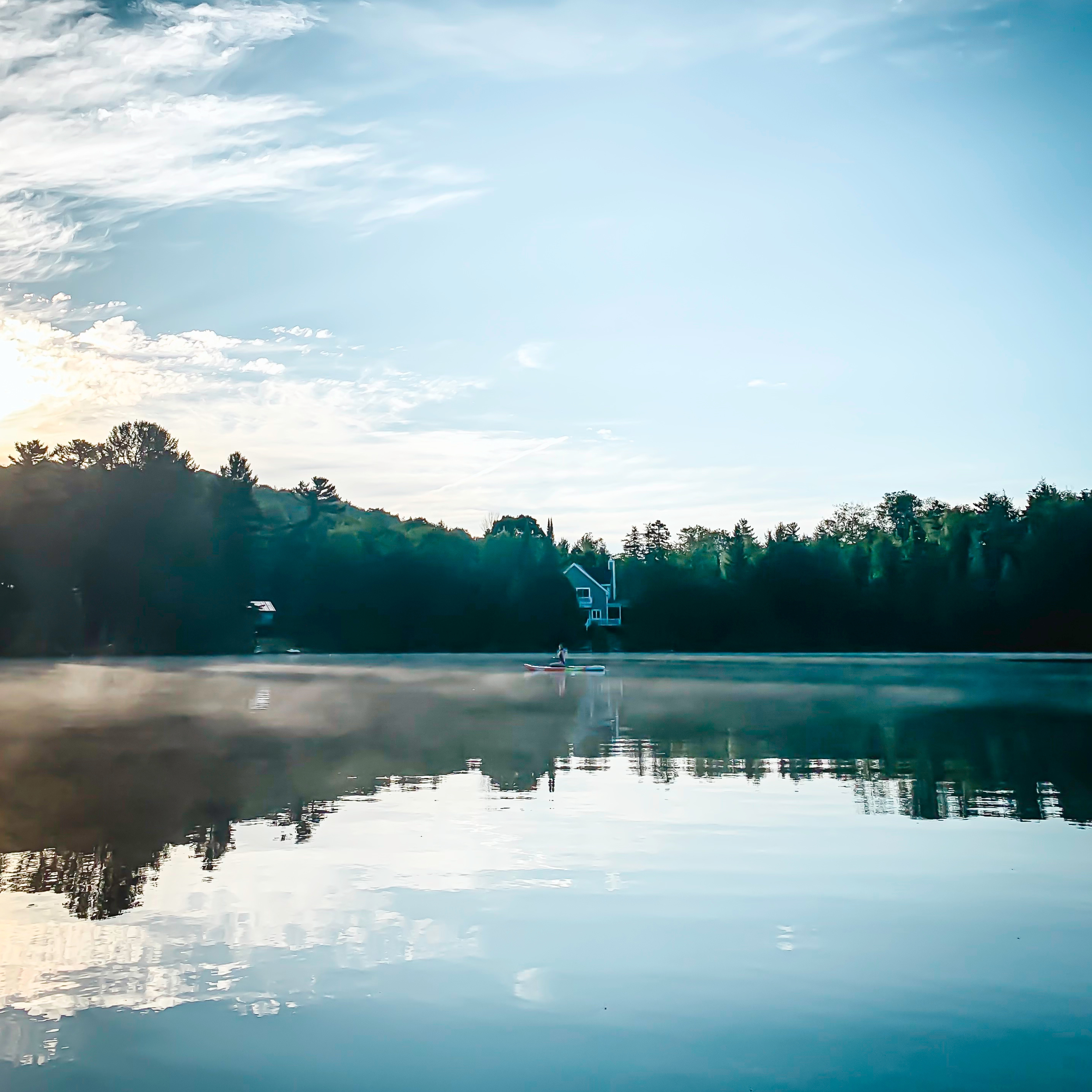 Serene view of Gratten Lake, Quebec, with lush trees and a charming cottage reflected on the calm water, with gentle steam rising from the surface